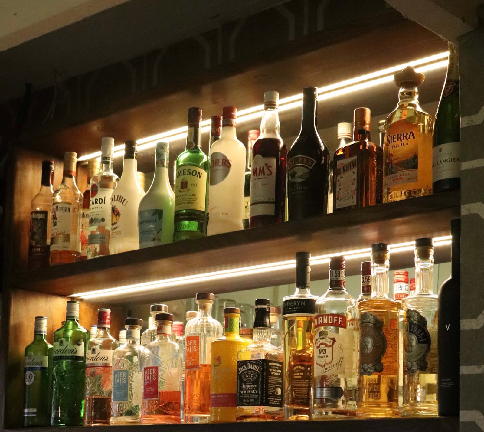Abbasi’s back bar — spirits lit on warm timber shelves against the octagon wallpaper