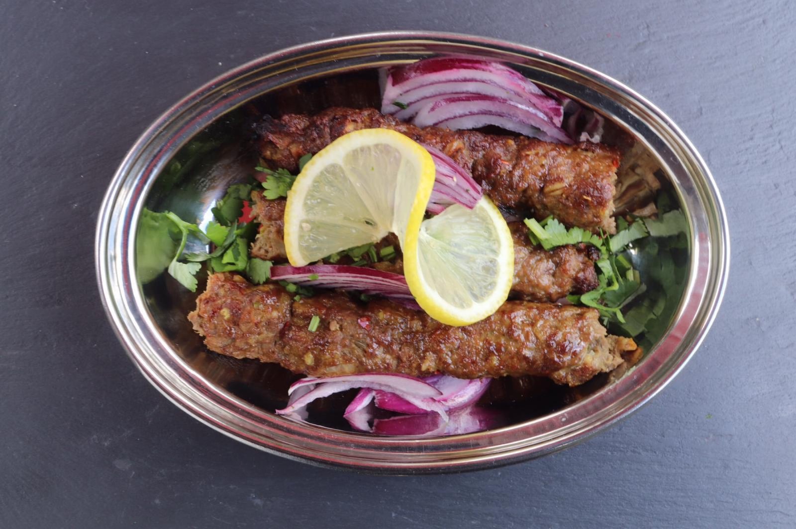 Seekh kebab skewers charred over fire, resting on dark slate