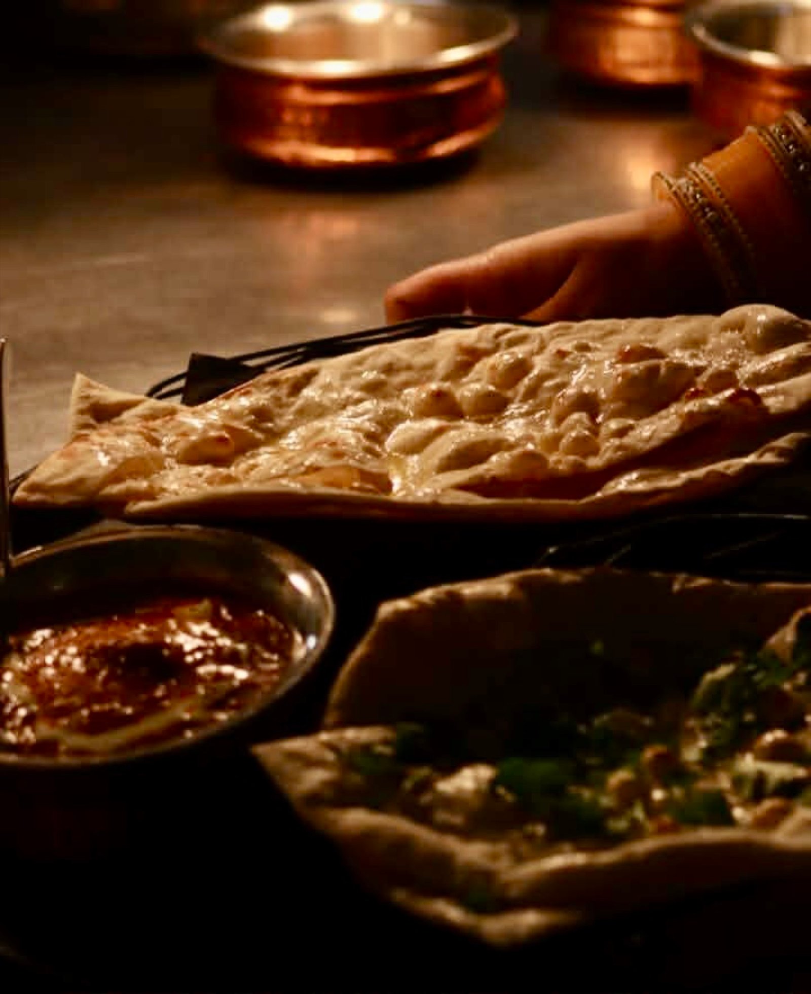 A hand reaching for fresh naan at the table